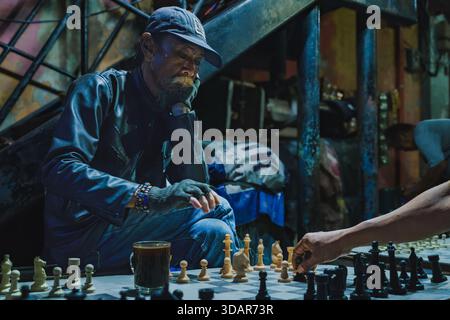 Balikpapan, Indonesien - 1. November 2025. Ein bärtiger Mann in einer Lederjacke beobachtet die Bewegung seines Gegners während eines Straßenschach-Spiels in der Nacht aufmerksam. Stockfoto