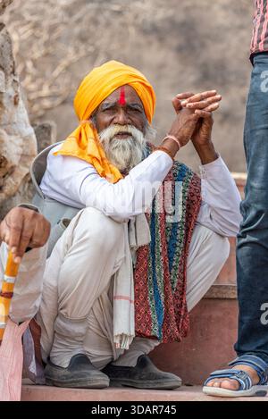 Älterer indischer Mann in Gelb Turban hockt draußen mit buntem gewebtem Tuch. Pushkar, Rajasthan, Indien, 28. Januar '24. Stockfoto
