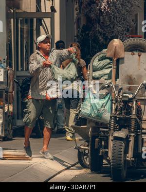 Ein offenes Straßenfoto eines Arbeiters, der Güter von einem modifizierten Lastenmotorrad an einem hellen Tag in Südostasien abwickelt. Stockfoto