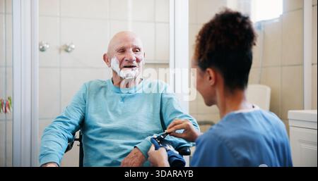 Seniorenmann, Krankenschwester und Rasiercreme im Badezimmer mit Rollstuhl, glücklich und sprechen mit der Pflege zu Hause. Personen, Pflegepersonen und ältere Menschen mit Stockfoto