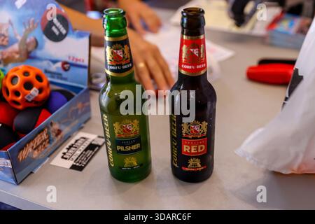 Zwei Flaschen griechisches Bier auf einem Tisch drinnen, auf dem grüne und braune Glasflaschen mit Etiketten während des zwanglosen Essens zu sehen sind. Stockfoto
