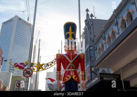 Melbourne, VIC, Australien. Dezember 2025. - Eine leuchtende rote Nussknacker-Soldat-Straßendekoration steht prominent auf der Bourke Street, eingerahmt von einem Mo Stockfoto