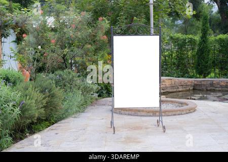 Eine weiße, leere Plakatwand auf einem Stand, isoliert vor einem grünen Gartenhintergrund. Die Hintergrundstruktur eines leeren Modellschilds bietet Platz für individuelle Anpassungen Stockfoto