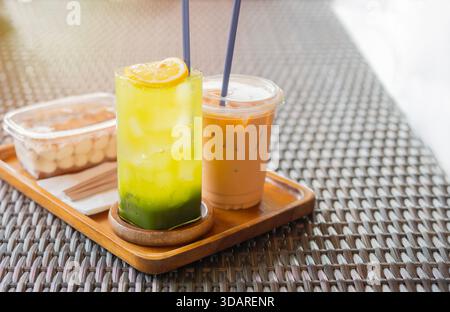 Ein köstliches süßes Essen mit Matcha Green Tea, frischer Zitrone, Eiskaffee und etwas Kuchen, serviert auf einem hölzernen Schneidebrett. Stockfoto