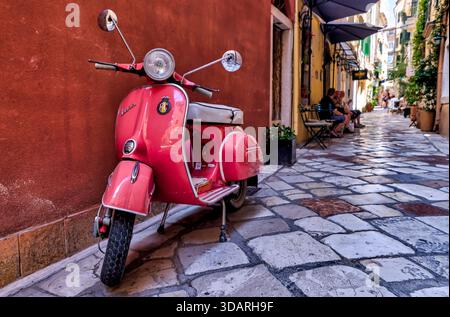 Roter Roller parkt auf einer Kopfsteinpflasterallee in der Altstadt von Korfu, Korfu, Griechenland, eingerahmt von historischen Gebäuden und engen Gassen. Stockfoto