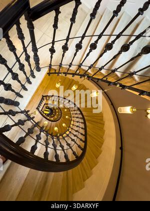 Wendeltreppe von oben betrachtet Eisenbalustrade Kurven um warme Glühbirnenbeleuchtung Marmortreppen leuchten elegante architektonische Innenräume erinnern an Luxus-Mystery-Einladung zu erkunden Stockfoto