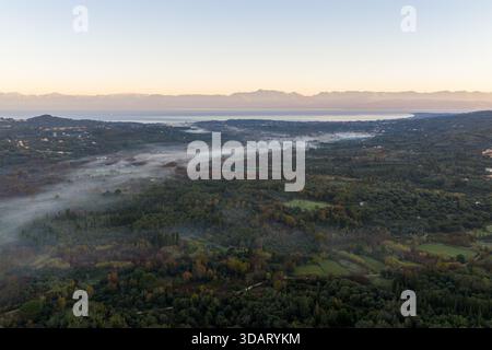 Breites Luftpanorama der Nordkorfu-Küste mit entfernten albanischen Bergen. Nebel schlängelt sich durch das Tal zum Meer bei Sonnenaufgang. Stockfoto