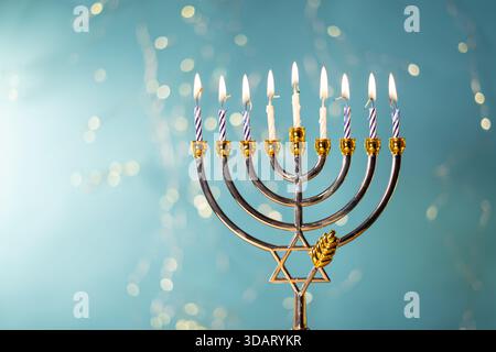 Eine goldene Menora mit neun beleuchteten Kerzen steht vor einem hellblauen Hintergrund und symbolisiert die Hanukkah-Feier. Stockfoto