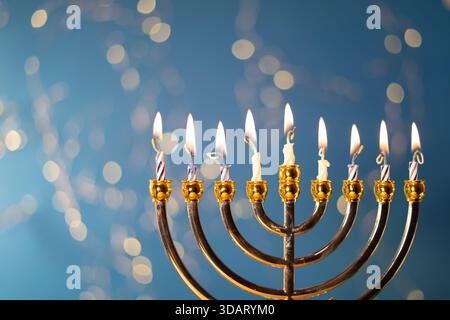 Eine goldene Menora mit neun beleuchteten Kerzen steht vor einem hellblauen Hintergrund und symbolisiert die Hanukkah-Feier. Stockfoto