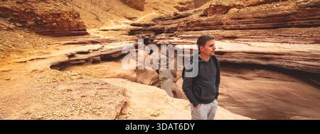 Trockenes Flussbett, Wildnis. Natürliche Wüstenlandschaft. Sandsteinstruktur. Junger Mann, der im Red Canyon in der Negev-Wüste in der Nähe von Eilat, Israel, spaziert. Stockfoto