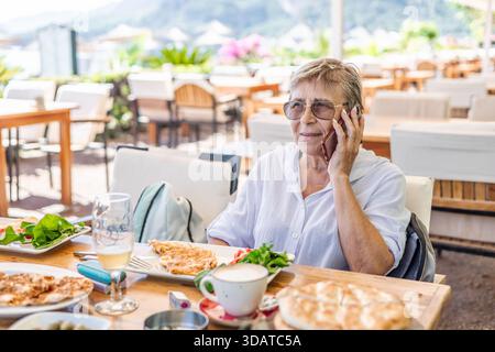 Eine ältere Frau mit Telefon sitzt im türkischen Restaurant am Strand Stockfoto