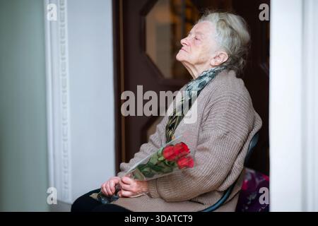 Ältere Frau, die auf einem Stuhl sitzt und einen Rosenstrauß trägt Stockfoto
