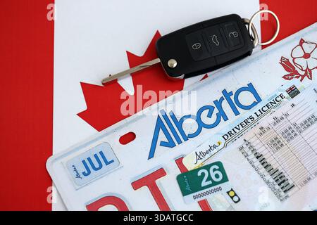 Alberta canadian Autokennzeichen und Zündschlüssel auf der Flagge von Kanada Nahaufnahme. Führerschein- und Zulassungskonzept Stockfoto