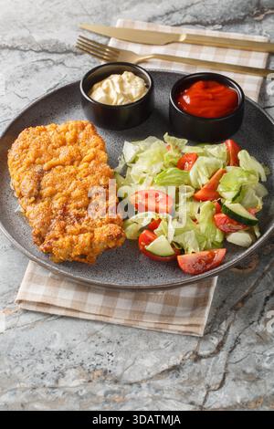 Sizilianisches paniertes Rindersteak, serviert mit frischem Salat und zwei Saucen in Nahaufnahme auf einem Teller auf dem Tisch. Vertikal Stockfoto