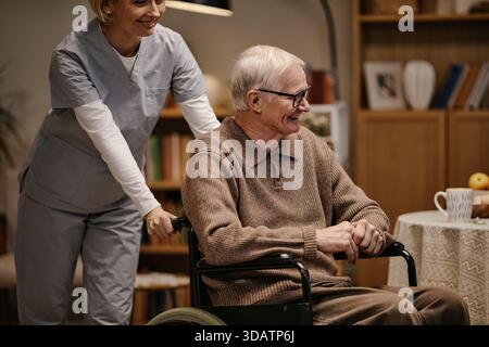 Kaukasischer Seniorenmann Lächelt, Während Die Krankenschwester Im Haus Rollstuhl Schiebt Stockfoto