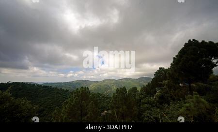 Blick auf sanfte grüne Hügel, bedeckt mit dichtem Wald unter einem dramatischen, bewölkten Himmel, mit blauen Flecken durch Islamabad, Islamabad Capital T Stockfoto