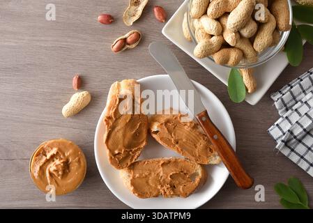 Frisch geschnittene ​​bread mit Erdnussbutter auf einem weißen Teller auf einem braunen hölzernen Küchentisch mit Obst und Gemüse. Draufsicht. Stockfoto