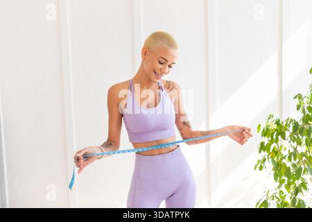 Gewichtsverlust-Konzept. Aufgeregte Dame, die ihre Taille misst und mit einem Lächeln auf Band blickt, Kopierraum Stockfoto