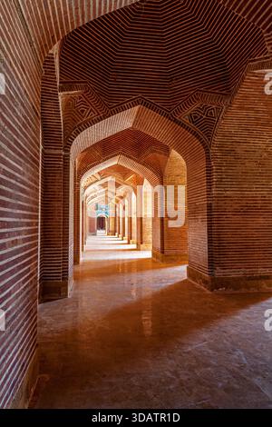Blick auf einen Korridor aus Bögen mit rotem Ziegelwerk und komplizierten Mustern, die in die Ferne führen, in warmes Licht getaucht, Thatta, Sindh, Pakistan. Stockfoto