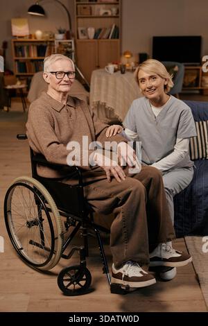 Senior-kaukasischer Mann mit Behinderung sitzt im Rollstuhl und lächelt Krankenschwester Stockfoto