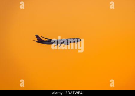7. Dezember 2025 Sotschi, Russland. Passagierflugzeug Nordwind fliegt vor dem Hintergrund eines hellen Sonnenunterganghimmels Stockfoto