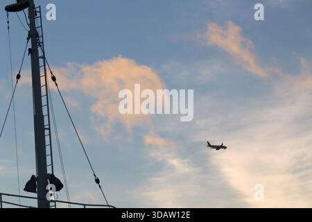 Das Flugzeug fliegt über einem Schiffsmast vor einem farbenfrohen Sonnenuntergangshimmel Stockfoto