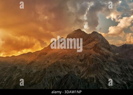 Aus der Vogelperspektive auf zerklüftete Gipfel, die einen feurigen Sonnenuntergang durchstechen, Triglav, Gorenjska, Slowenien. Stockfoto