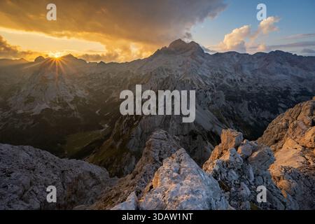 Aus der Vogelperspektive auf die zerklüfteten Gipfel der Julischen Alpen, die einen feurigen Sonnenuntergangshimmel durchdringen und lange Schatten über die zerklüftete Landschaft werfen, Triglav, Gorenjska, Stockfoto