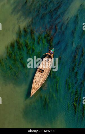 Aus der Vogelperspektive eines hölzernen Bootes, das durch das türkisfarbene Wasser inmitten der lebendigen grünen Wasserpflanzen schneidet, Sirajganj, Rajshahi Division, Bangladesch. Stockfoto