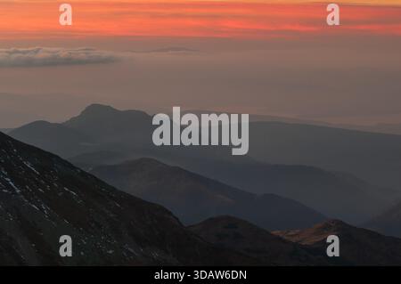 Aus der Vogelperspektive auf die dramatischen, geschichteten Berge, die in dunklen Tönen gemalt sind, mit den Gipfeln, die das schwindende Licht durchdringen, von Bystra, Zilina Region, Slo Stockfoto
