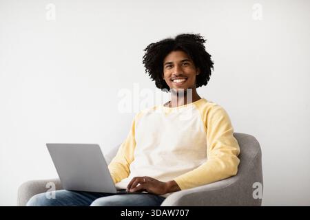 Der lächelnde Schwarze Mann genießt Fernarbeit, während er bequem zu Hause sitzt Stockfoto