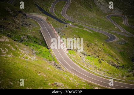 Blick auf die gewundene Transfăgărășan-Straße, die sich durch die lebhaften grünen Hügel schlängelt, ein Asphaltband, das durch die rumänische Landschaft Poien führt Stockfoto