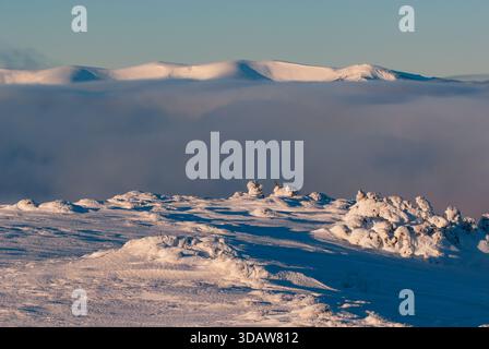 Blick auf eine schneebedeckte Landschaft mit einem Wolkenmeer, eingebettet unter fernen Bergen, getaucht in den sanften Glanz des Sonnenlichts, Velka Hola, Banska Bystric Stockfoto