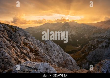 Aus der Vogelperspektive auf zerklüftete, felsige Gipfel treffen auf den goldenen Himmel, Sonnenlicht durchdringt durch Wolken über den Bergen, Tosc, Gorenjska, Slowenien. Stockfoto