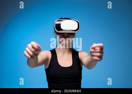 Lächelnde Frau mit VR-Headset und erweiterten Armen, die in einer immersiven digitalen blauen Umgebung interagieren Stockfoto