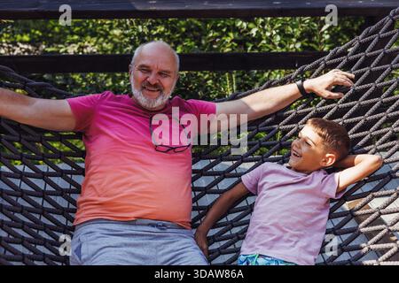 Ein fröhlicher Großvater und Enkel, der einen sonnigen Tag in einer Hängematte genießt. Sie teilen Lachen und Wärme und verkörpern das entspannende Wesen der Familie Stockfoto