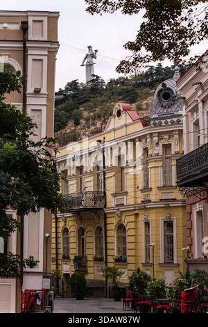 Malerische Aussicht auf eine bezaubernde Tiflis Straße mit der berühmten Mutter von Georgien, die auf einem Hügel im Hintergrund thront und eine Mischung aus historischen Elementen zeigt Stockfoto