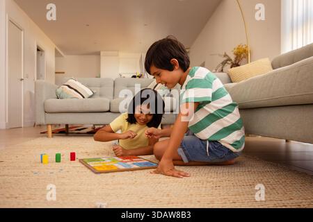 Zwei Kinder beteiligen sich fröhlich an einem Brettspiel auf einem gemütlichen Wohnzimmerboden und zeigen Teamarbeit, Konzentration und Spaß in einem hellen, einladenden h Stockfoto