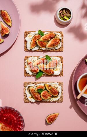 Blick von oben auf Toast mit Feigen mit Frischkäse und Pistazien auf einem rosafarbenen Teller. Begleitet von Feigen, Nüssen und Honig. Ein köstliches, frisches Frühstück Stockfoto