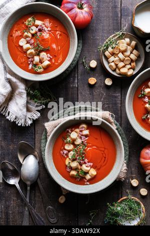 Herzhafte Tomatensuppe garniert mit Croutons und frischen Kräutern, serviert in Keramikschüsseln. Eine gemütliche Herbstmahlzeit auf einem rustikalen Holztisch mit Löffeln Stockfoto