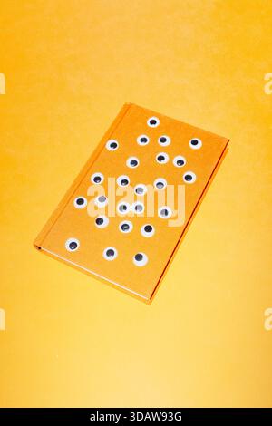 Ein skurriles konzeptionelles Bild mit einem Buch mit mehreren Googly-Augen auf dem Cover, kreativ auf einem leuchtend gelben Hintergrund platziert, das visio symbolisiert Stockfoto