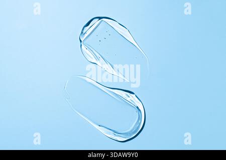 Nahaufnahme klarer Abstriche der Geltextur, künstlerisch auf einem ruhigen blauen Hintergrund angeordnet. Die durchsichtigen Abstriche weisen kleine Blasen auf, die betonen Stockfoto