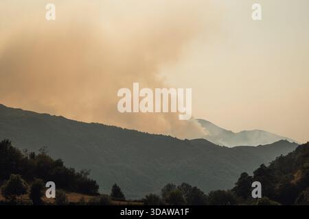 Rauch steigt sanft in den Himmel über einem ruhigen, bewaldeten Tal in der Abenddämmerung in Valle de Somiedo, Asturien, Spanien, und schafft ein stimmungsvolles und atmosphärisches A Stockfoto