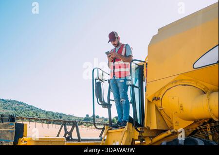 Ein Landwirt in Guadalajara, Spanien, verwendet ein Smartphone auf einem Mähdrescher inmitten malerischer Felder. Das Bild zeigt die Mischung aus moderner Technologie Stockfoto