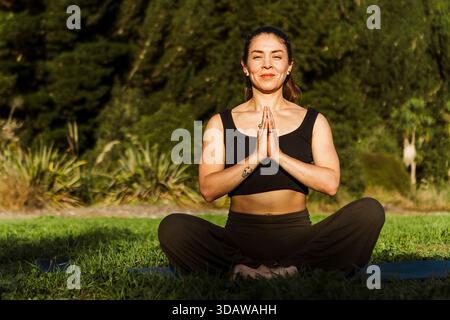 Eine Frau, die im Herbst in Neuseeland Yoga in einer ruhigen Umgebung im Freien praktiziert. Sie sitzt friedlich auf einem grasbewachsenen Feld, umgeben von üppigem Grün A Stockfoto