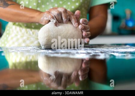 Zugeschnittene, nicht erkennbare Frau, die in einer modernen Küche Teig knete und zum Backen vorbereitet. Ihre Hände sind während ihrer Arbeit mit Mehl bedeckt. Stockfoto