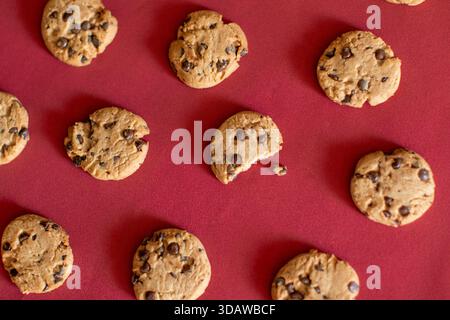 Eine Sammlung köstlicher hausgemachter Schokoladen-Chip-Cookies auf einem leuchtend roten Hintergrund. Die Kekse sind goldbraun, gefüllt mit reichhaltigem Schoko Stockfoto