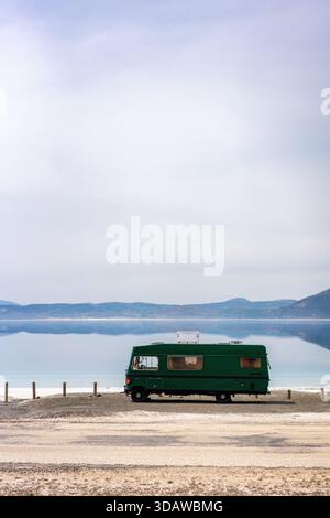 Eine ruhige Szene mit einem grünen Wohnmobil, der am Salda Crater Lake in der Türkei parkt. Das ruhige Wasser und die fernen Hügel schaffen eine malerische und friedliche Atmosphäre Stockfoto