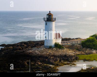 Aus der Vogelperspektive auf den scharf weißen Leuchtturm, der hoch über dem blauen Ozean steht, ein Leuchtfeuer der Hoffnung an der felsigen Küste, Gloucester, Massachusetts, United Stockfoto