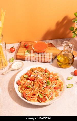 Ein Teller Spaghetti mit reichhaltiger Tomatensauce und geriebenem Parmesan, garniert mit frischem Basilikum. Begleitet von Olivenöl auf einem pfirsichfarbenen Backgr Stockfoto